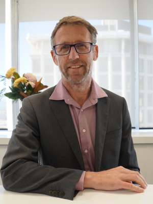 Head and shoulders portrait of Andrew Royle sitting at a desk with a window behind him.